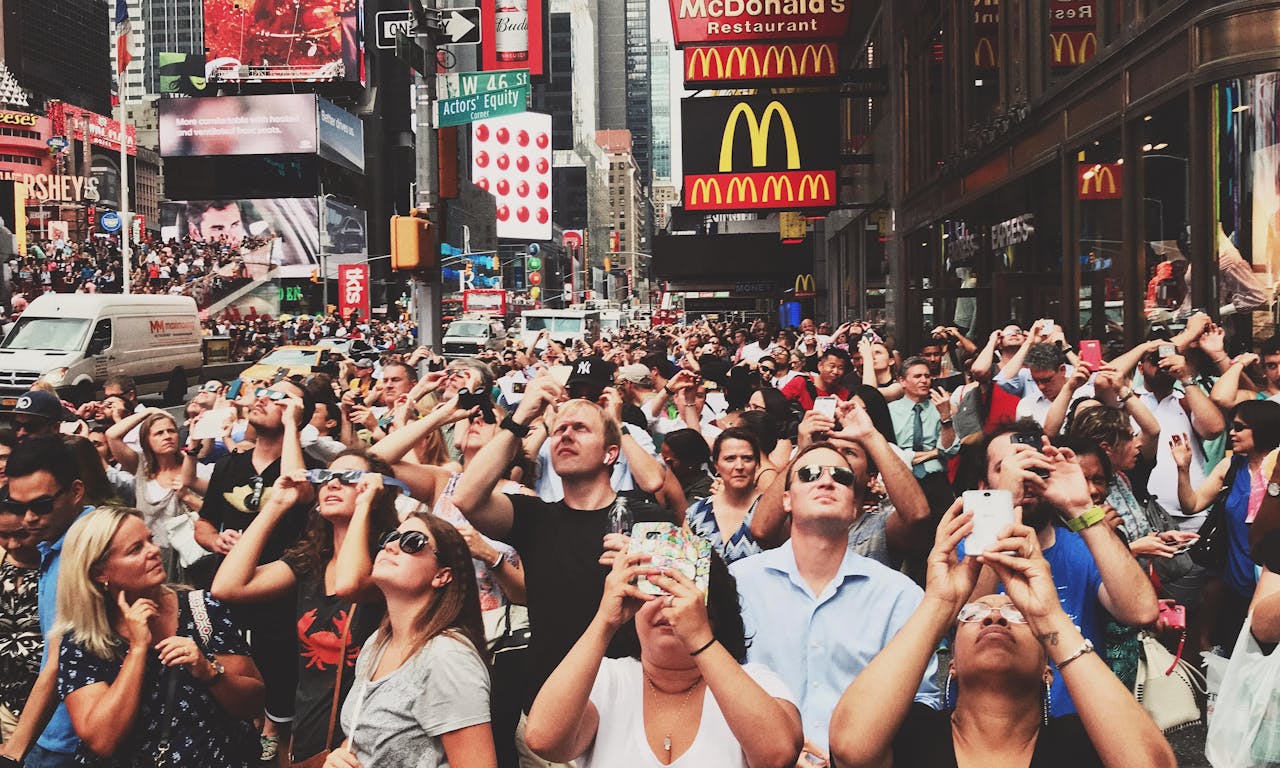 Diverse crowd in Times Square, New York City capturing moments with smartphones.
