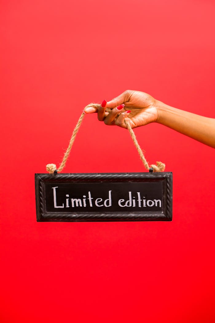 Close-up of a hand holding a limited edition sign against a striking red background.