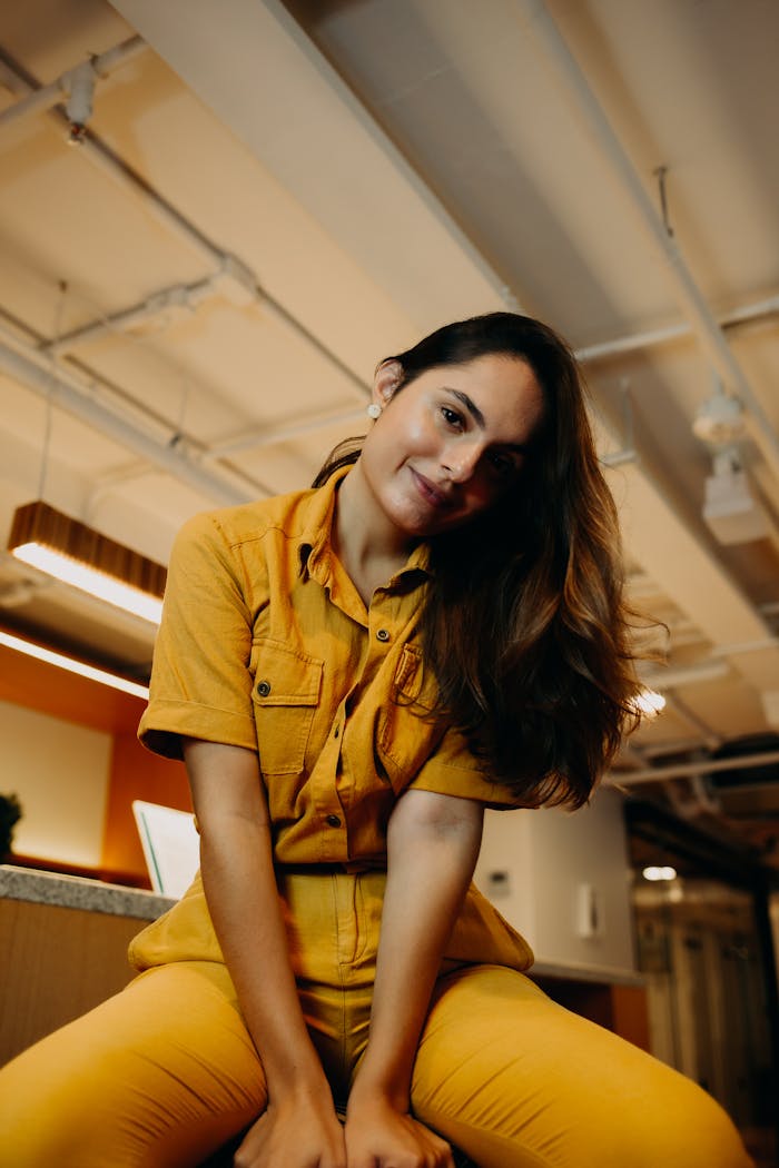 Portrait of a woman in yellow attire, posing indoors in a modern setting.