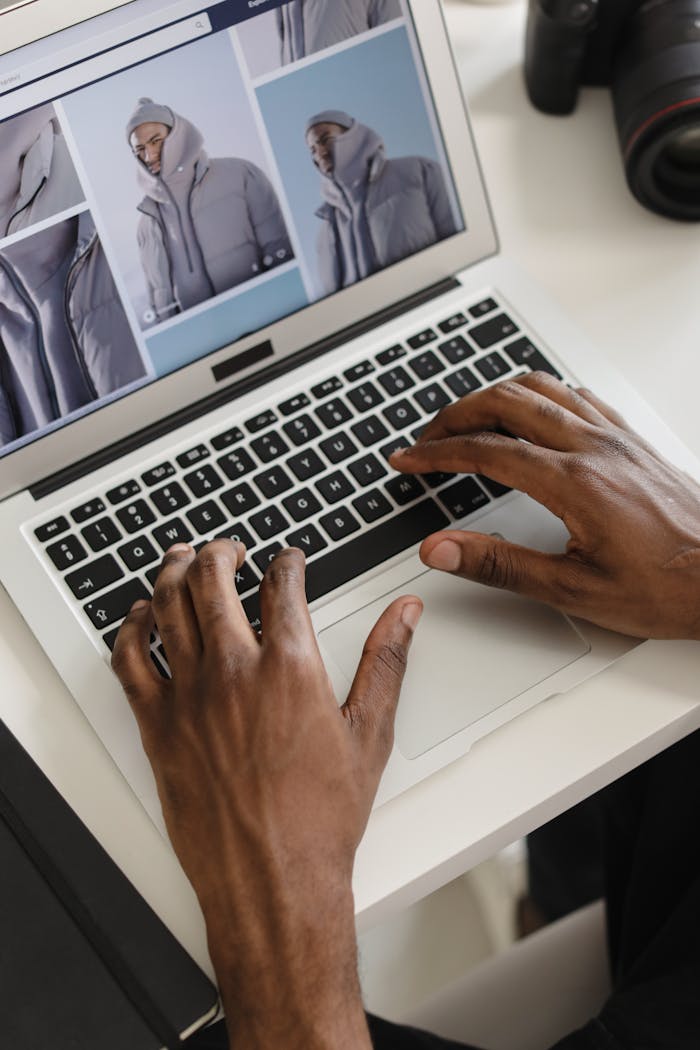Hands typing on a laptop displaying jacket images, perfect for e-commerce or fashion stock photos.